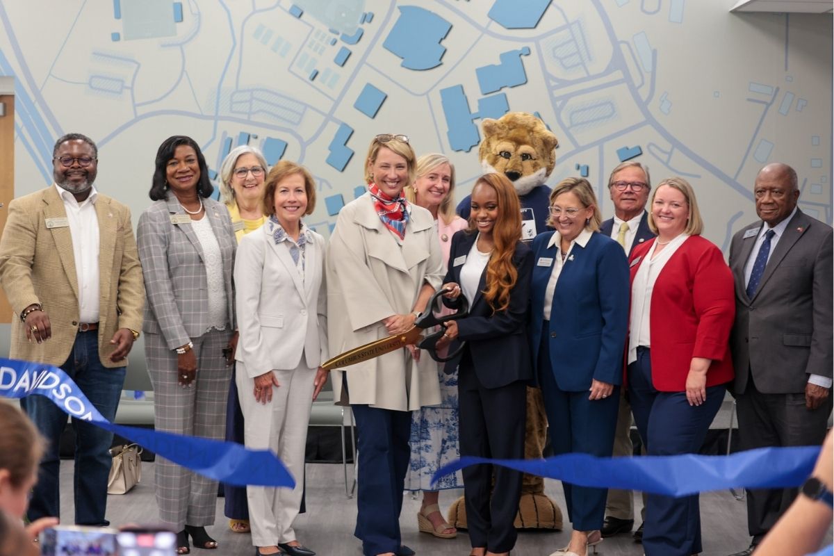 Administrators, elected officials a student and and the Cody the Cougar mascot gather indoors to cut the ceremonial blue ribbon for the Davidson Student Center re-opening.