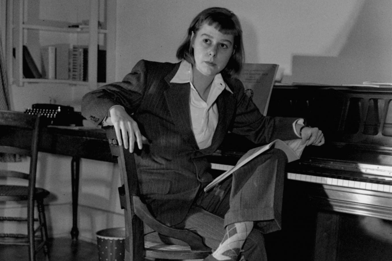 Black and white photo of Carson McCullers reading while seated at a piano