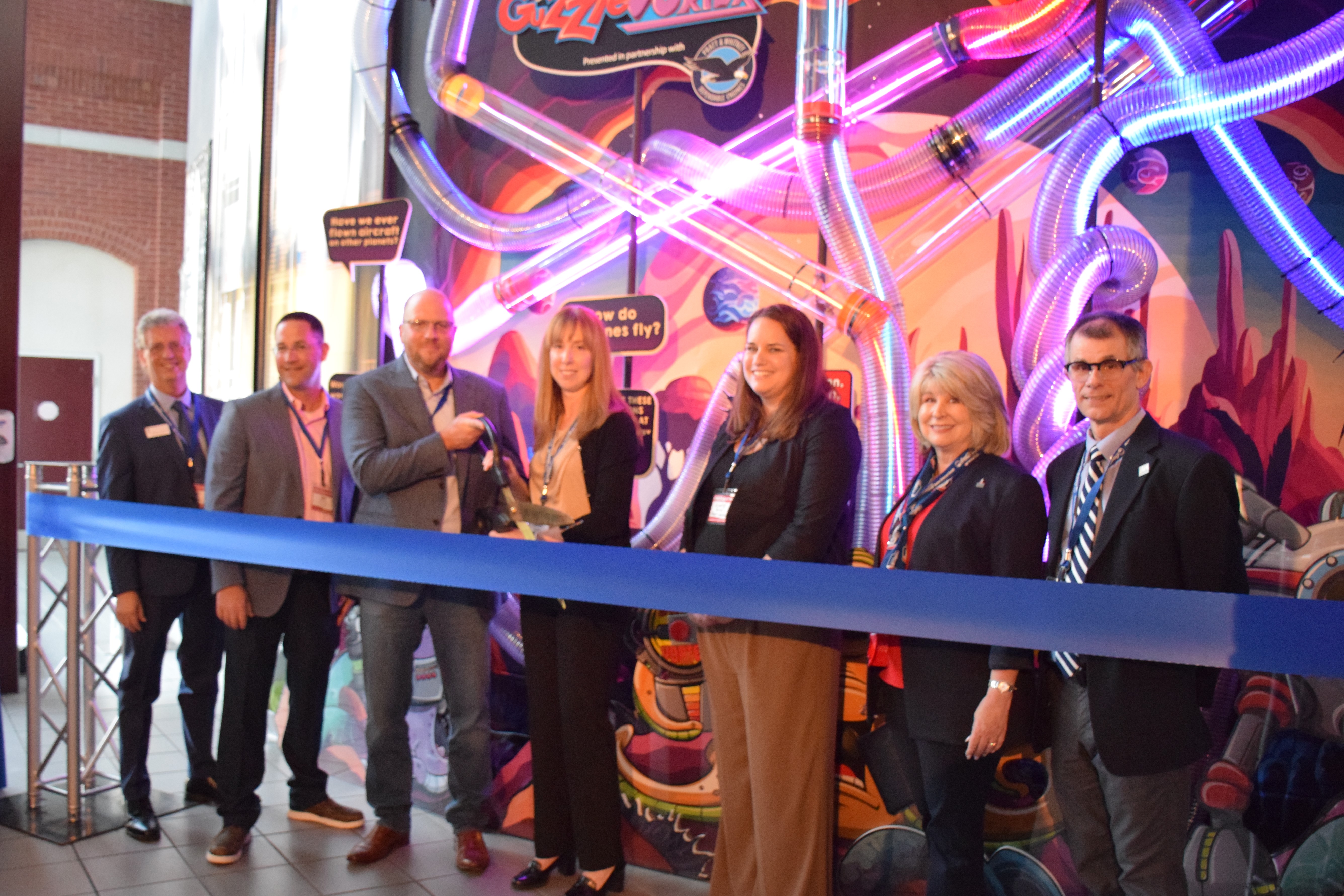 Group of people cutting a grand-opening ribbon with a large pair of scissors