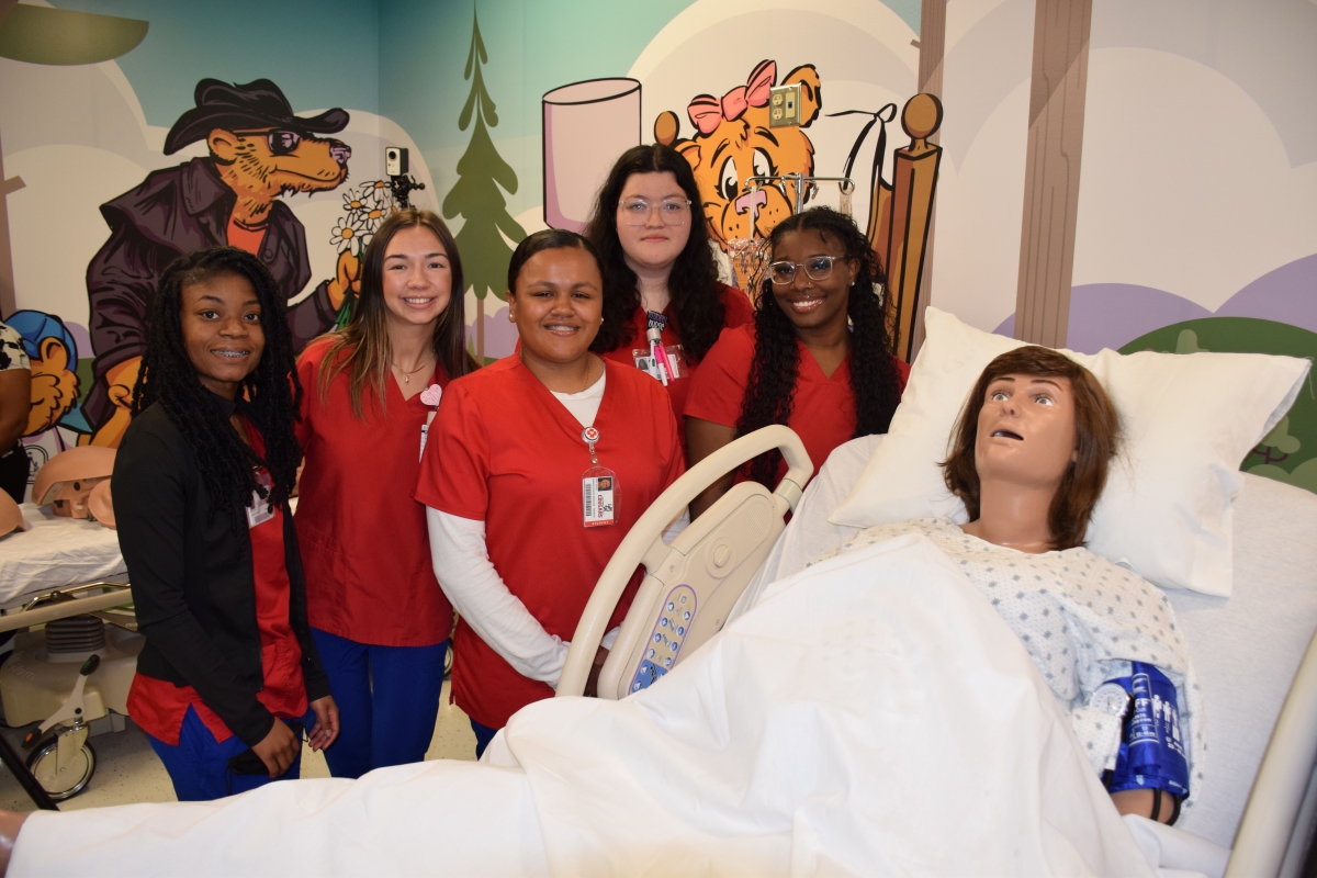 Group of nursing students standing bedside with a lifelike medical mannequin