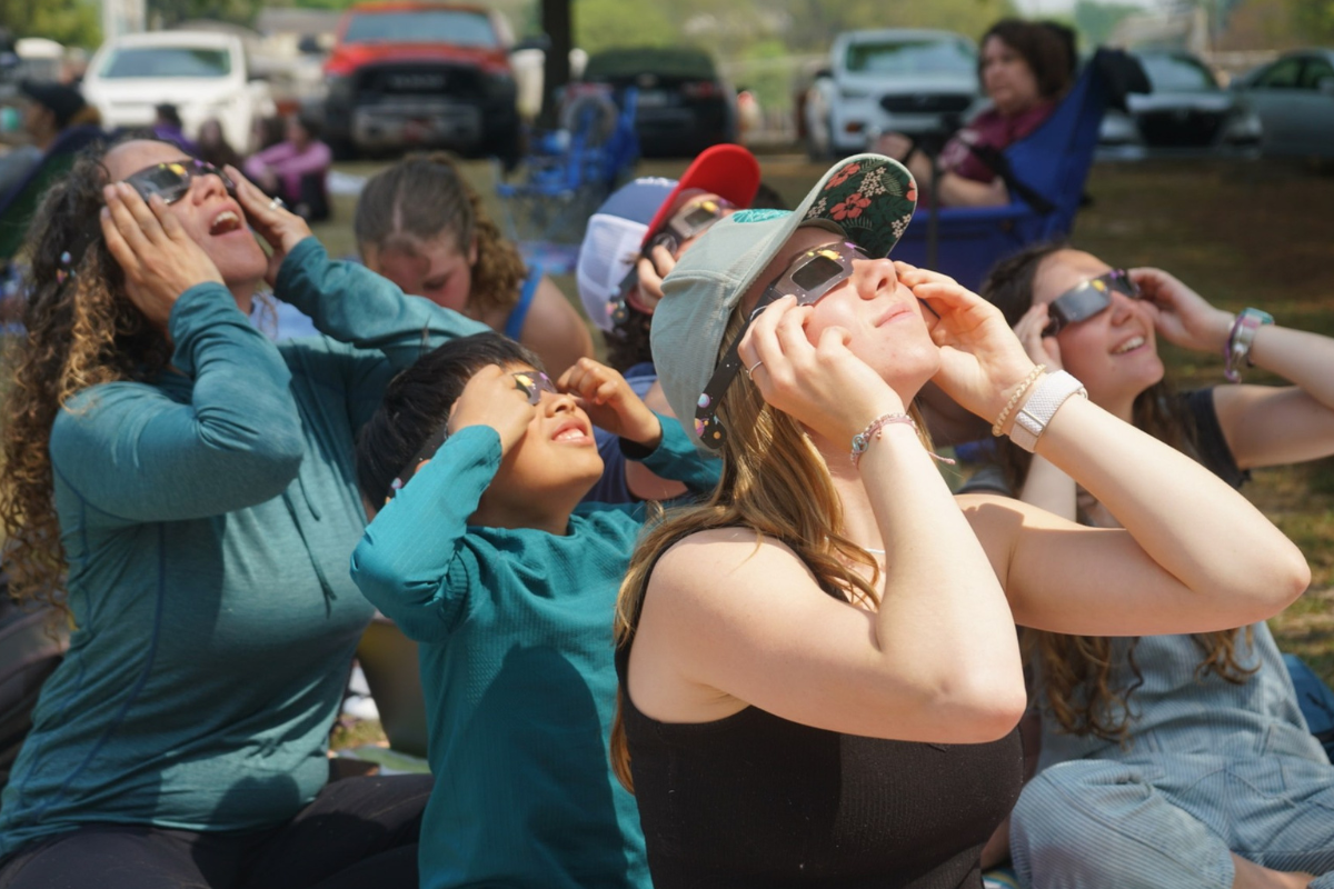A group of students looking at the solar eclipse wearing special eclipse-viewing glasses.