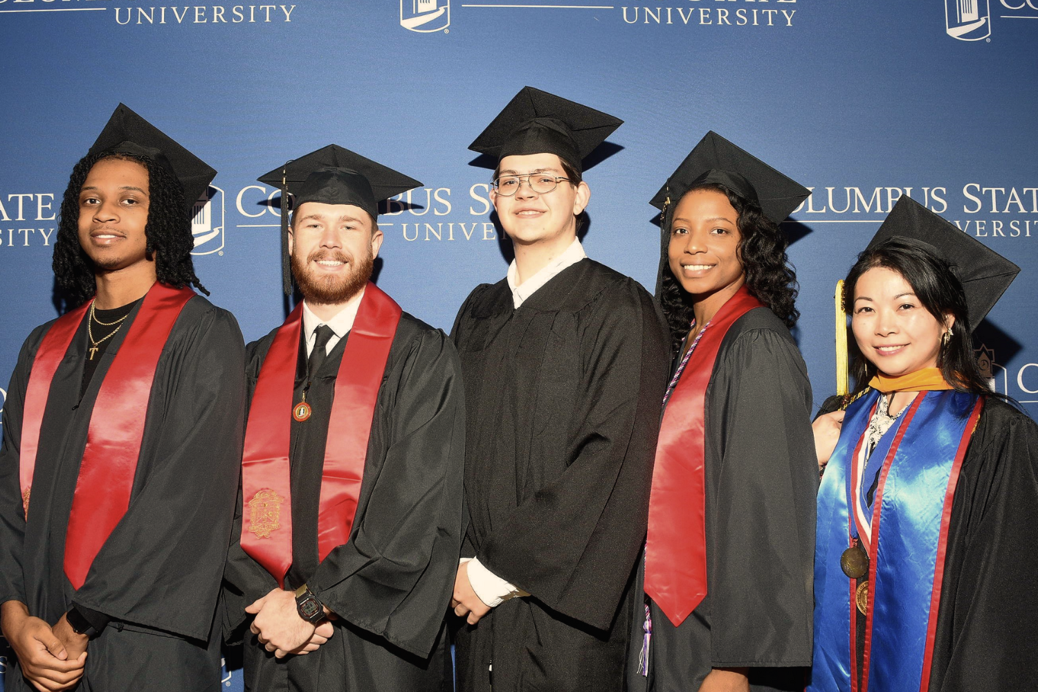 Group of graduates standing in front of a blue backdrop
