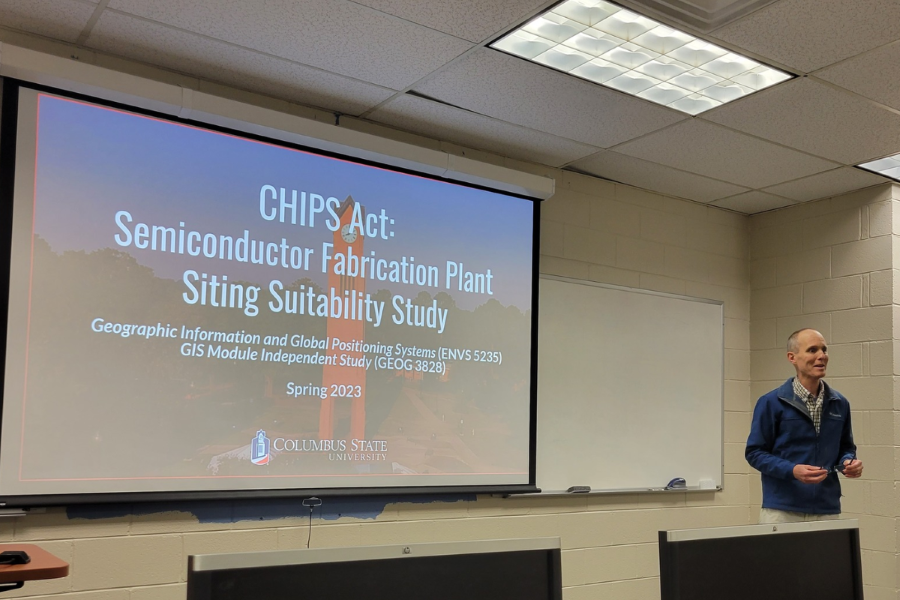 Dr. Troy Keller presents on his class' work with a presentation slide behind him titled: CHIPS Act: Semiconductor Fabrication Plan Siting Suitability Study