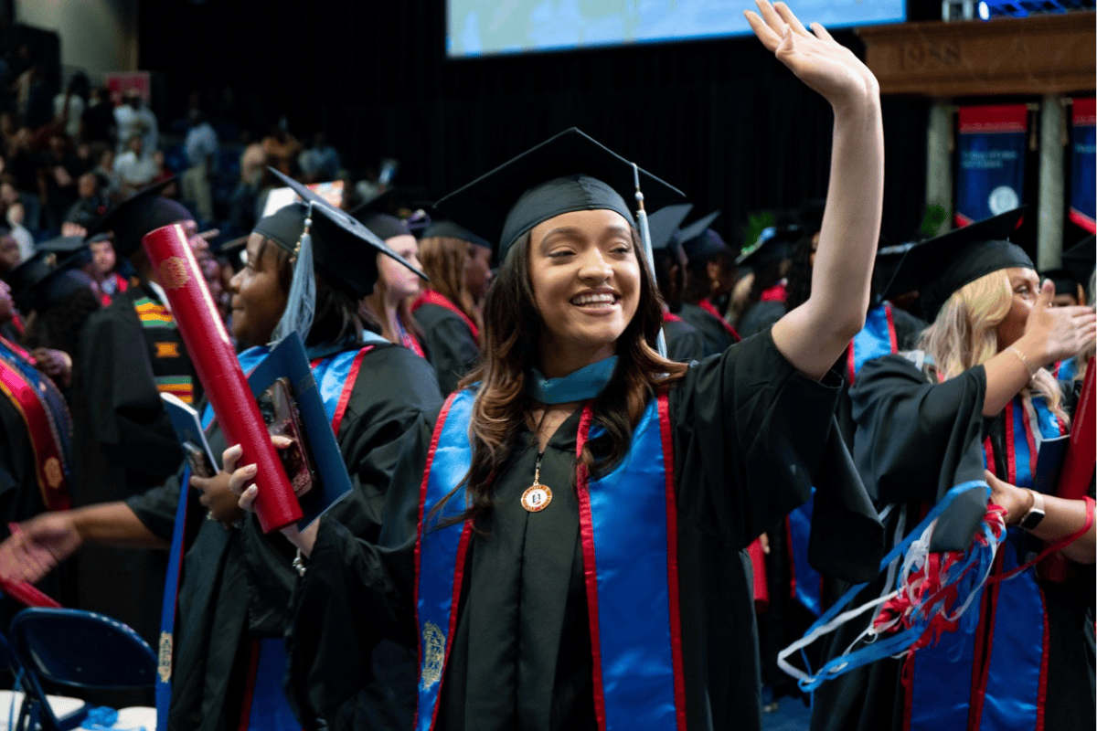 Picture of a college graduate waiving at a graduation ceremony