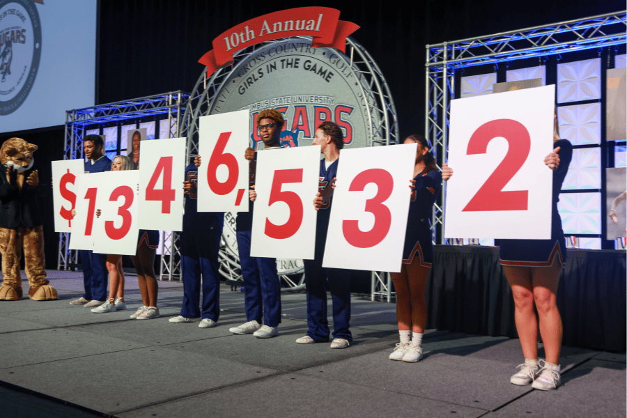 Student-athletes holding up placards with numbers that read $1,346,532.