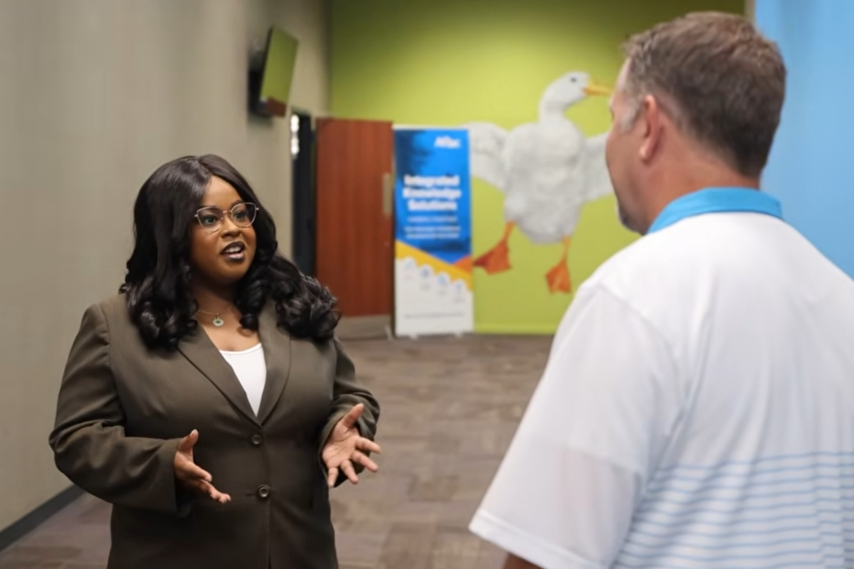 A Columbus State University student speaks with an Aflac executive during a corporate visit, with the Aflac duck mural displayed in the background.