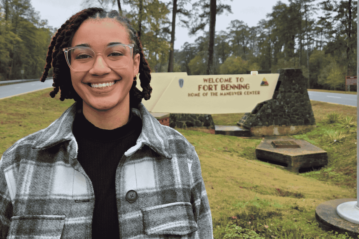 Johnson standing in front of a sign that reads: Welcome to Fort Benning, home of the Maneuver Center.