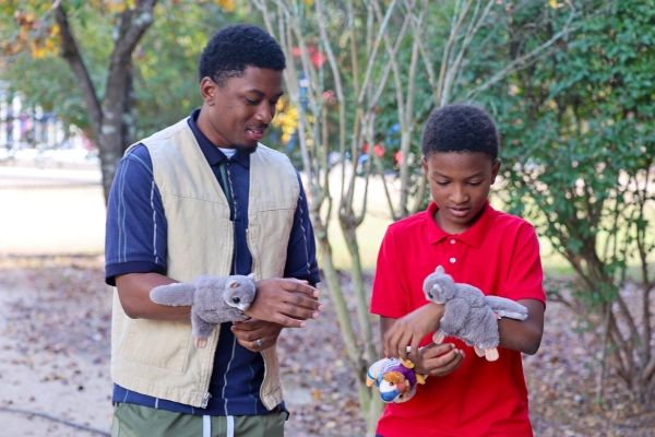 Armstrong and a student are wearing squirrel stuffed animals on their wrist and working together in an outside setting