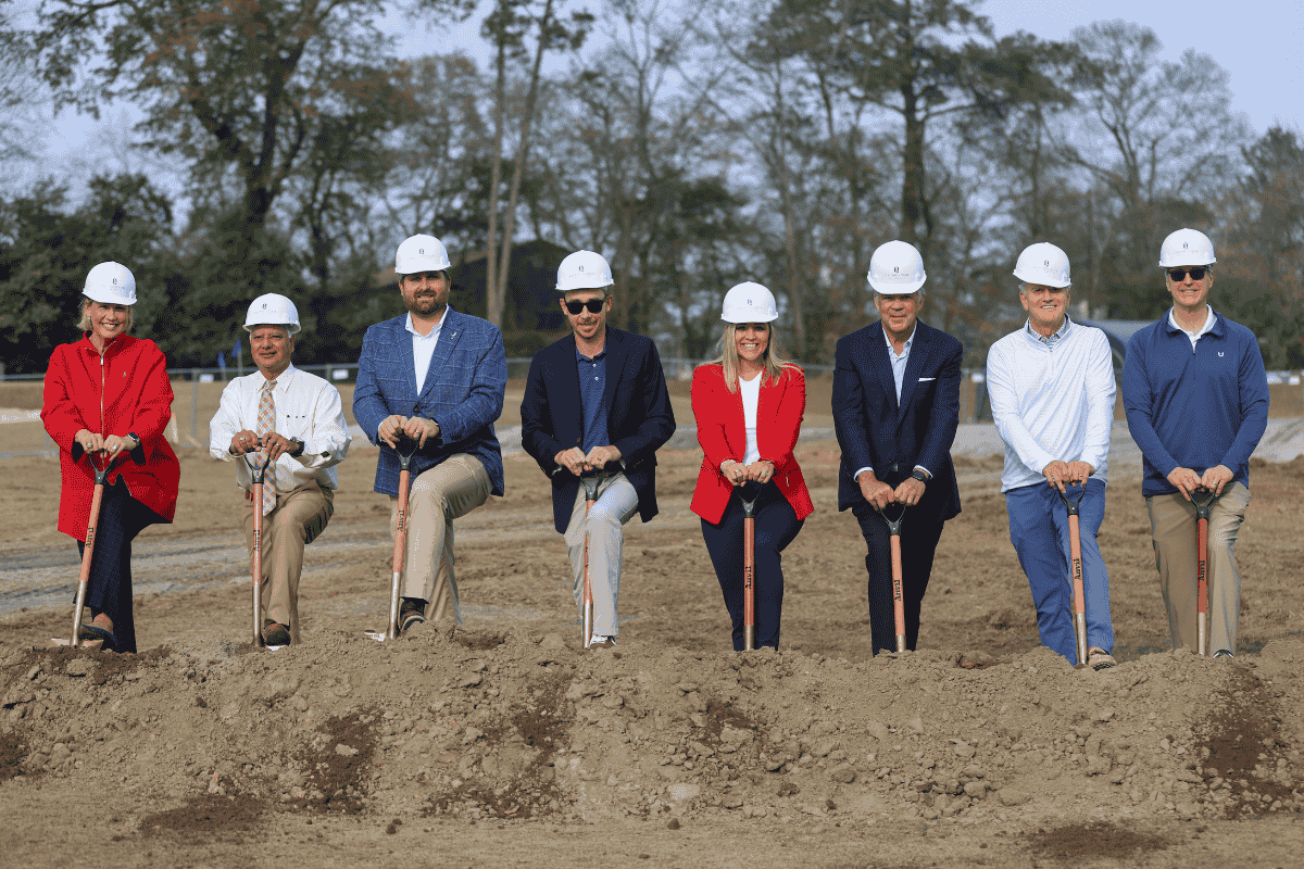 Group of people wearing hardhats and propped against shovels preparing to shovel dirt for a ceremonial ground-breaking