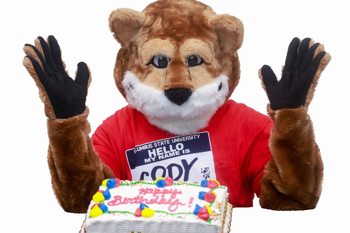 CSU mascot Cody the Cougar wearing a 'Hello My Name Is Cody' name tag behind a birthday cake that says 'Happy Birthday!