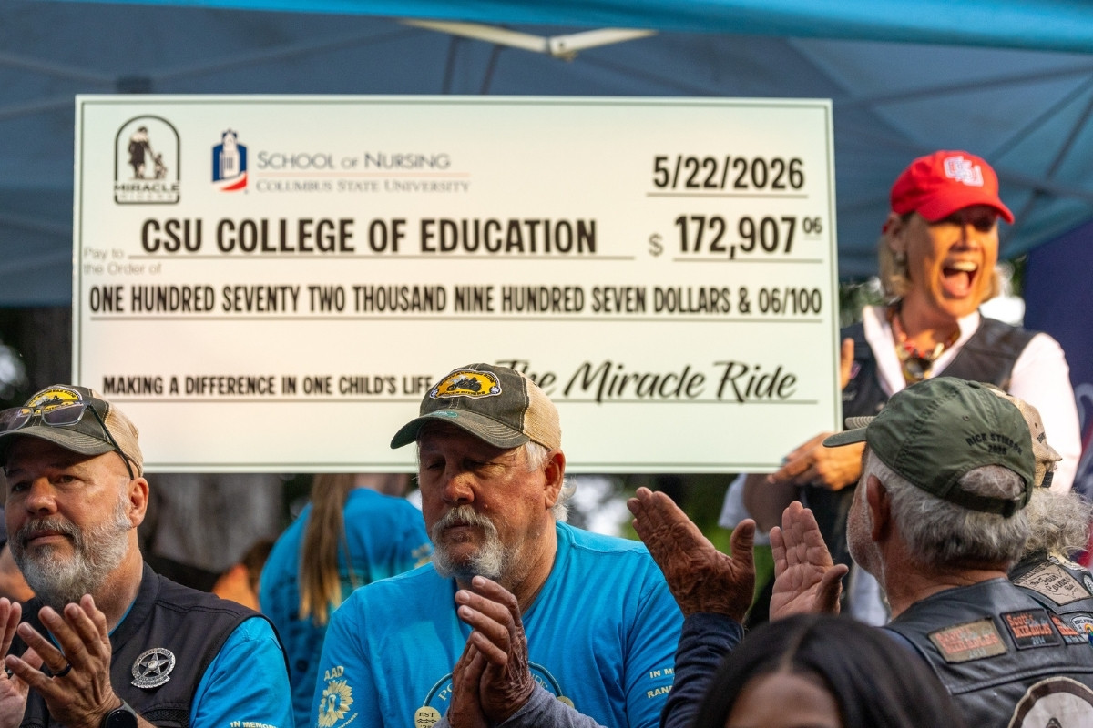 ​An outdoor event featuring a large presentation check held up in the background. The check is made out to 