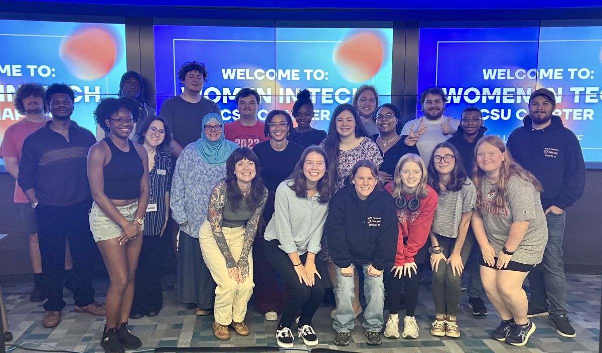 Dodson and her instructors and classmates taking a group photo in the TSYS Center for Cybersecurity in front of a display that reads "Welcome to Women in Tech"