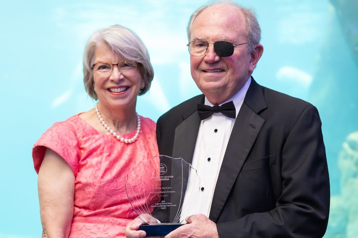 Steve Butler, wearing a tuxedo, poses with his wife as they hold his University System of Georgia Regents' Hall of Fame Alumni and Distinguished Friends Award for Columbus State University.