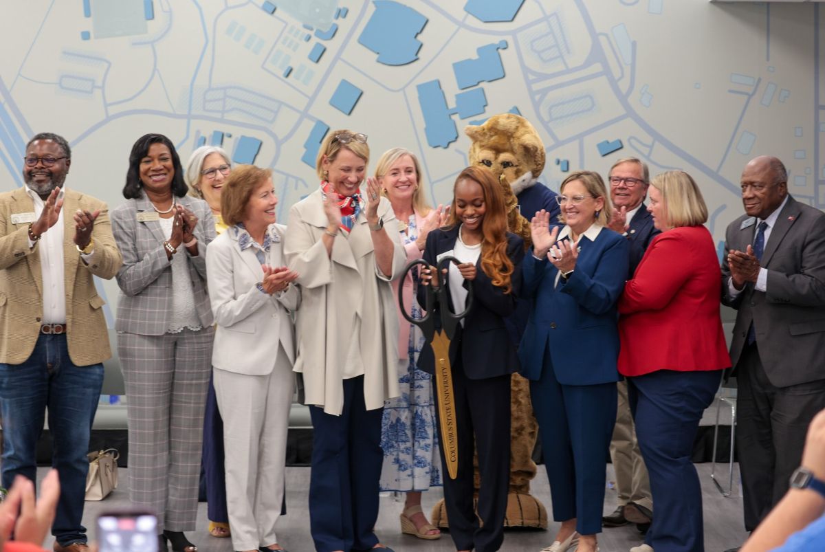 University administrators, elected officials, a student leader and the Cody the Cougar mascot gather indoors to cut the ceremonial blue ribbon for the Davidson Student Center re-opening.