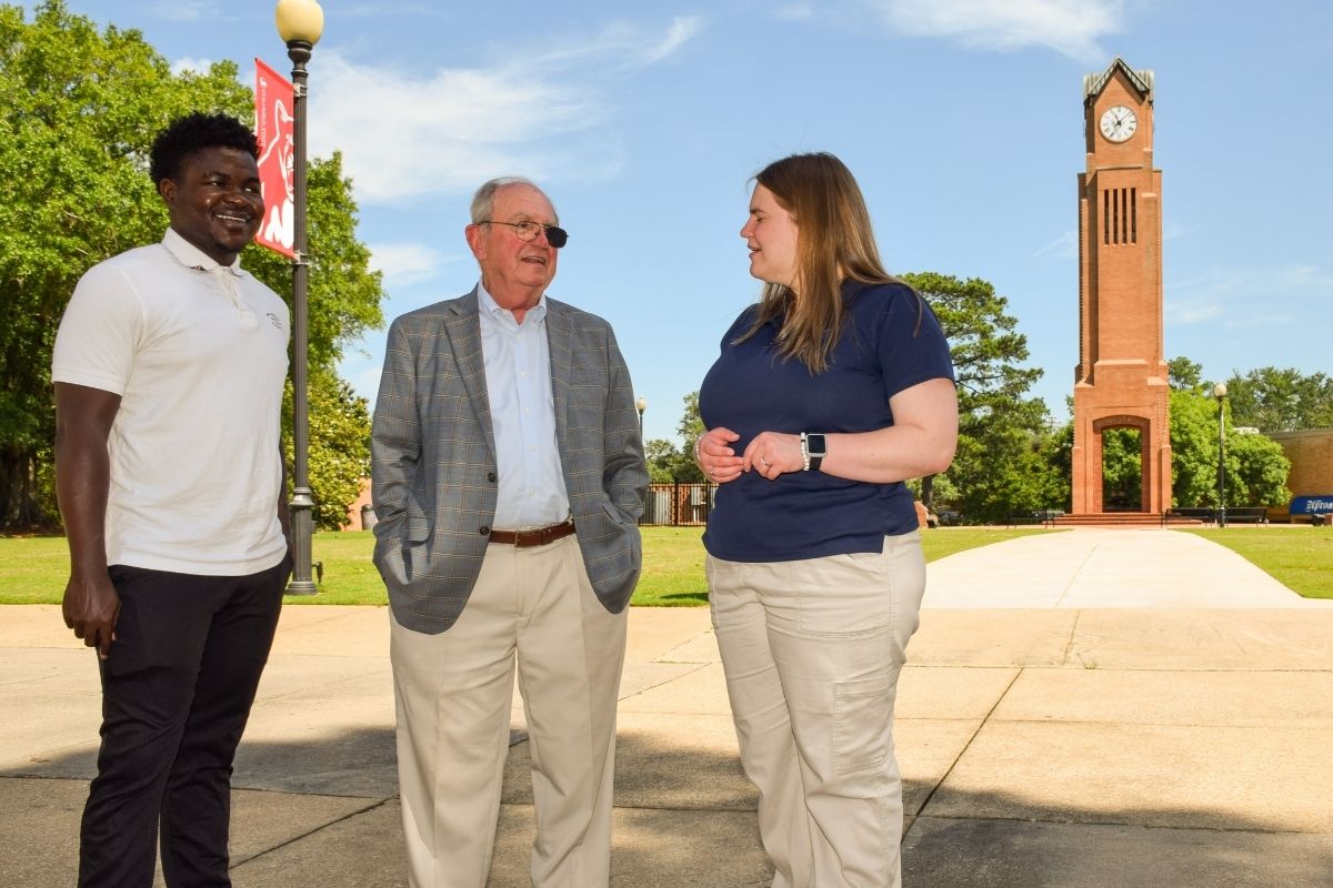 Steve Butler speaks with two university students on campus, with the Whitley Clock Tower visible in the background background.