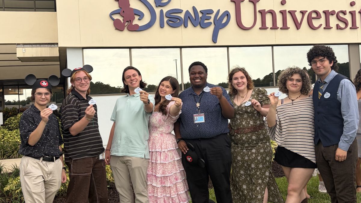 Columbus State University students participating in the Disney College Program pose together holding their official employee name tags outside the Disney University facility.