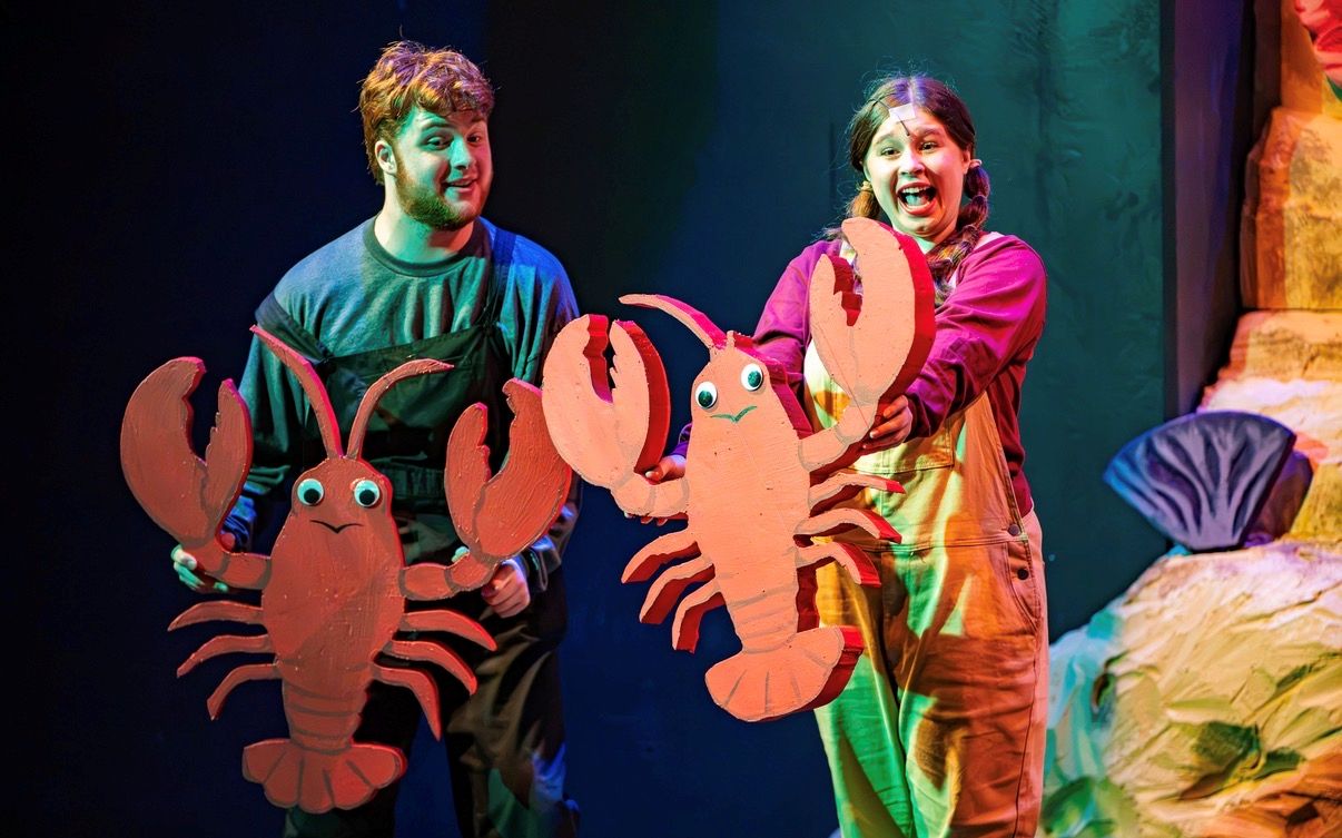 Farrar and a fellow theatre student manipulate vibrant lobster puppets during a live stage production.