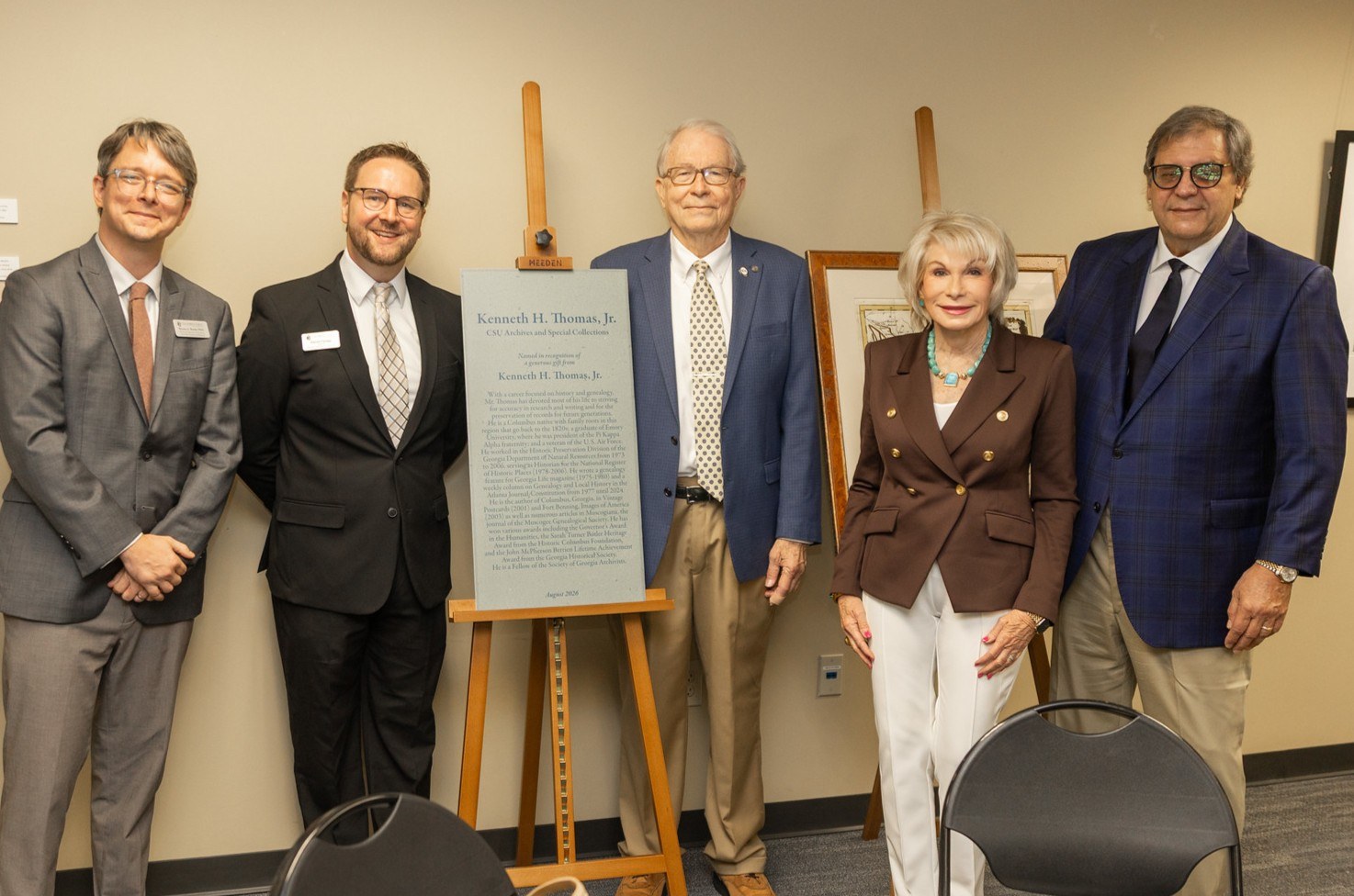 Group photo of Kenneth Thomas standing by a commemorative naming plaque, joined by university administrators and family members