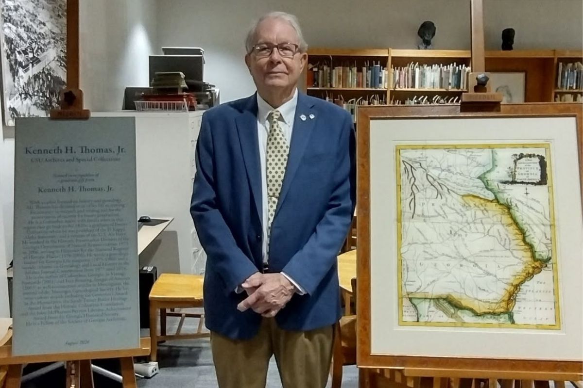 Kenneth Thomas Jr. standing in the Thomas Archives & Special Collections next to a commemorative naming plaque and a framed map