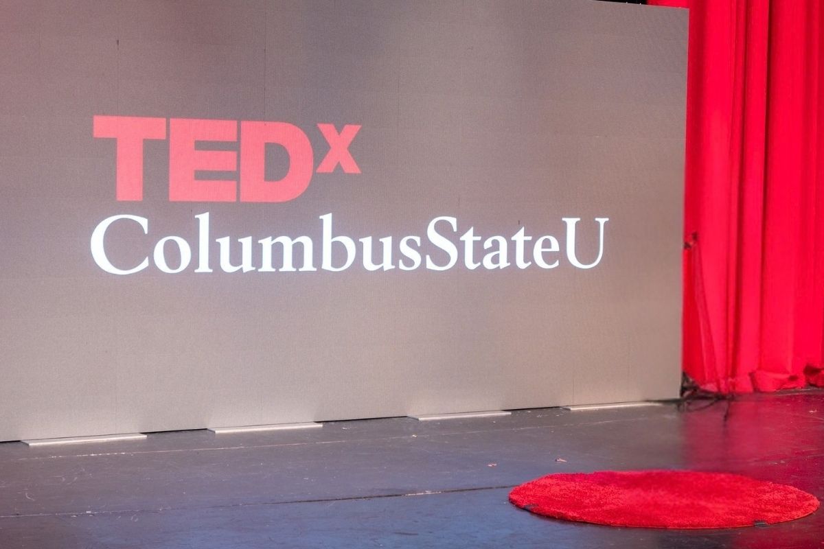 A stage setup for TEDxColumbusStateU featuring a large gray backdrop display with the red 