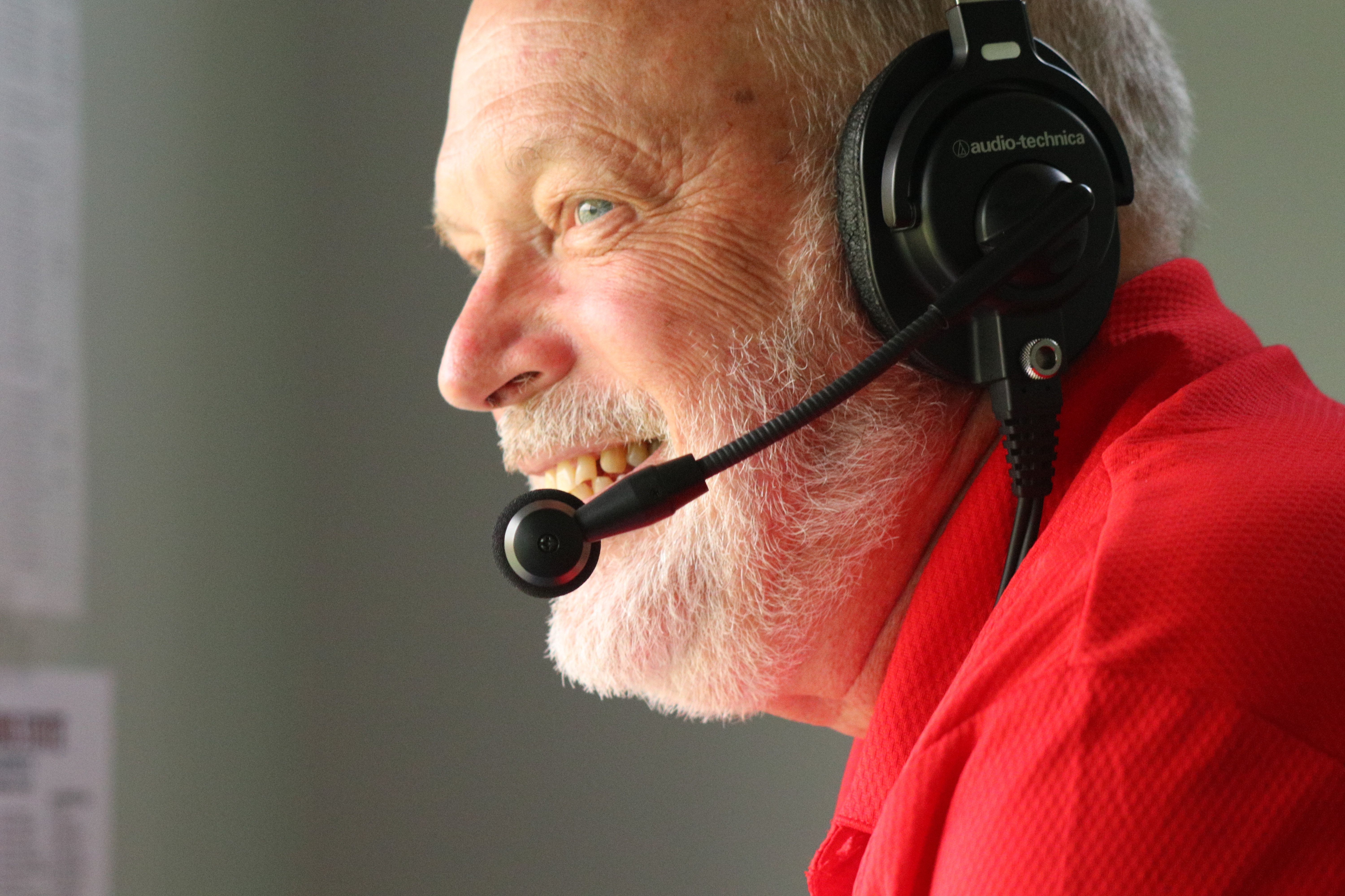 Close up of Miller looking towards left off camera wearing a black broadcasting headset with mic.