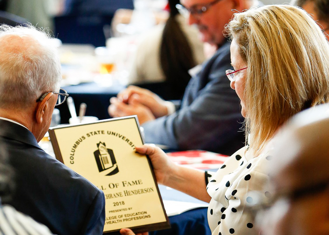 A man and woman at a table look at a gold plaque alumni award.