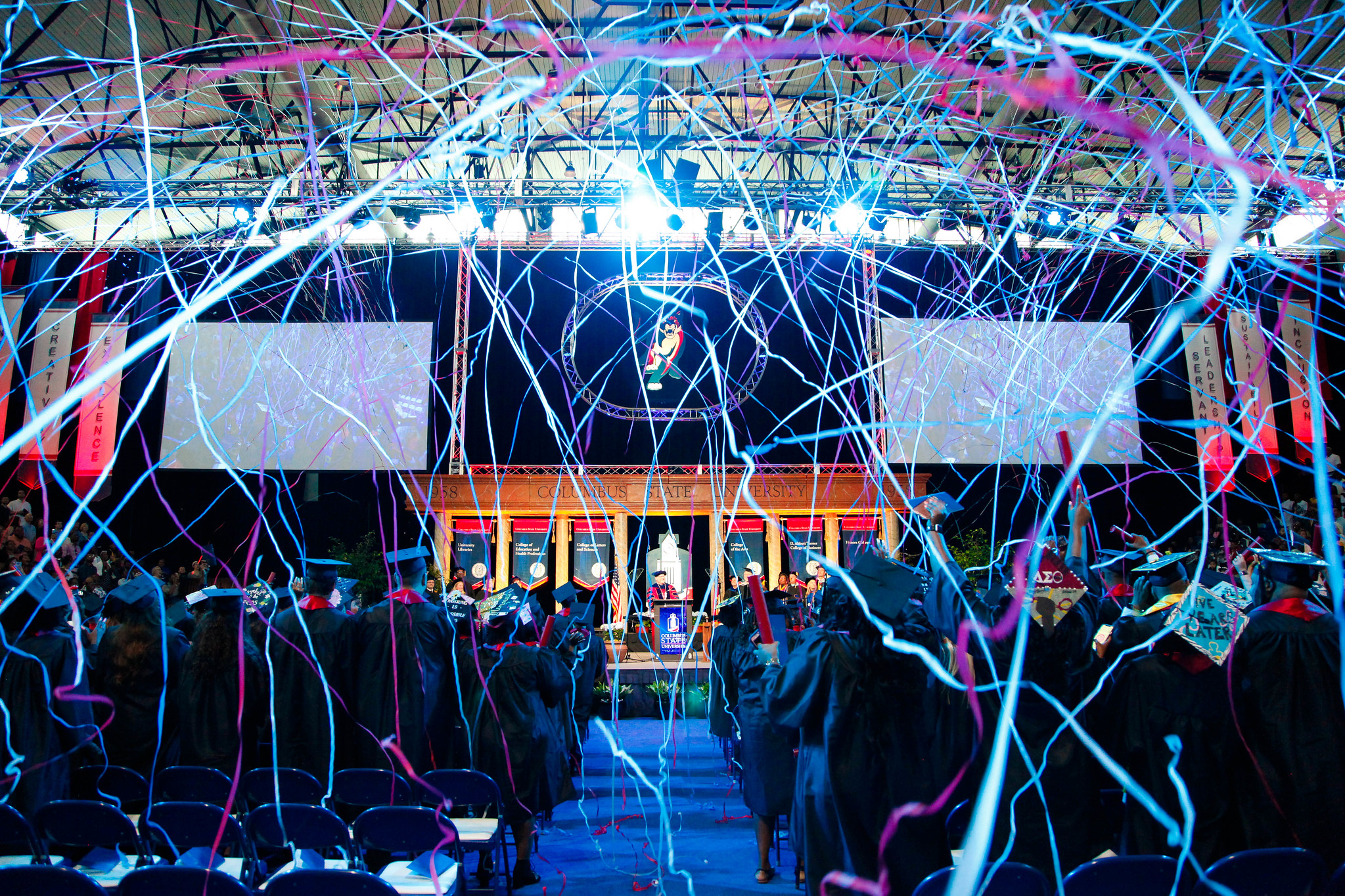 Red and blue streamers fall during an indoor graduation ceremony.