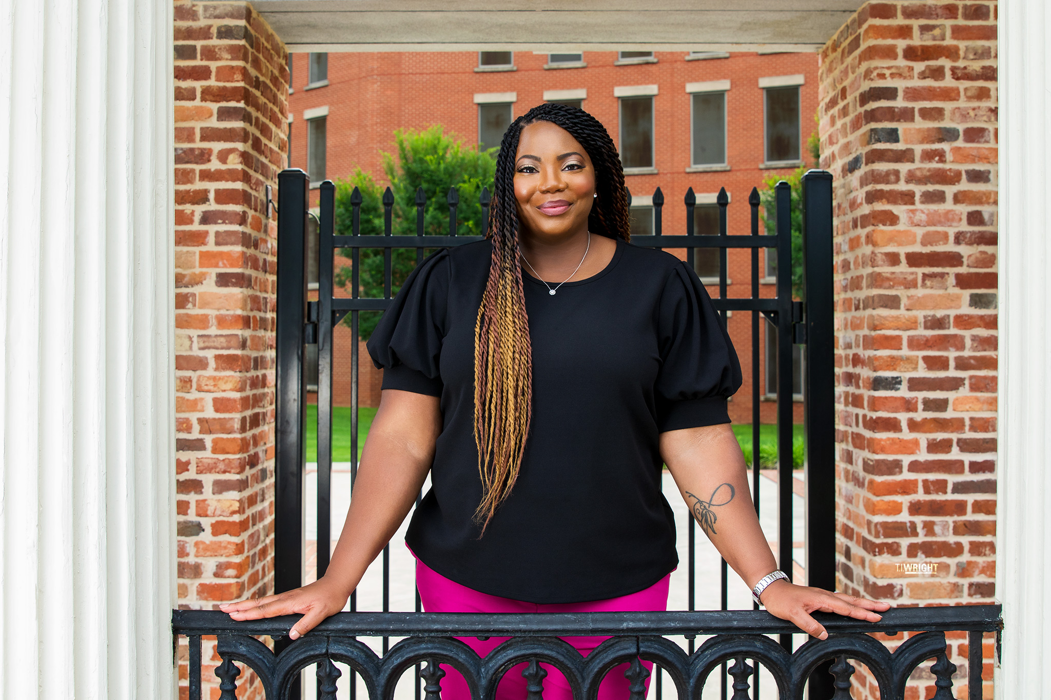 Raveeta Moore stands against a black fence outdoors wearing a black shirt and pink pants.